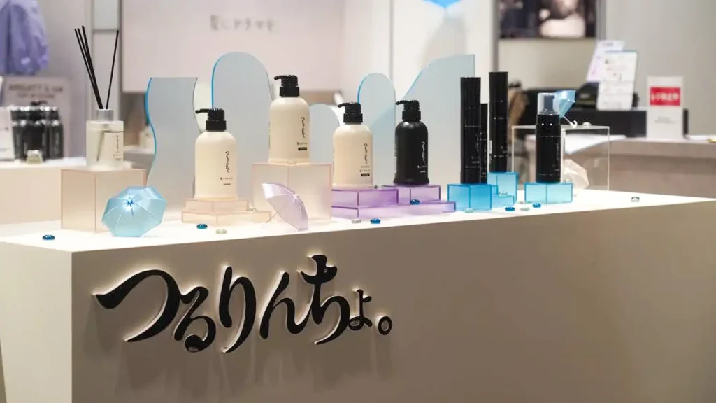 case_kaminidoramawo-03_08 | 株式会社ビーツ(BEEATS) Display of beauty products on a white counter with pastel bottles, accessories, and decorative blue props in a store window.